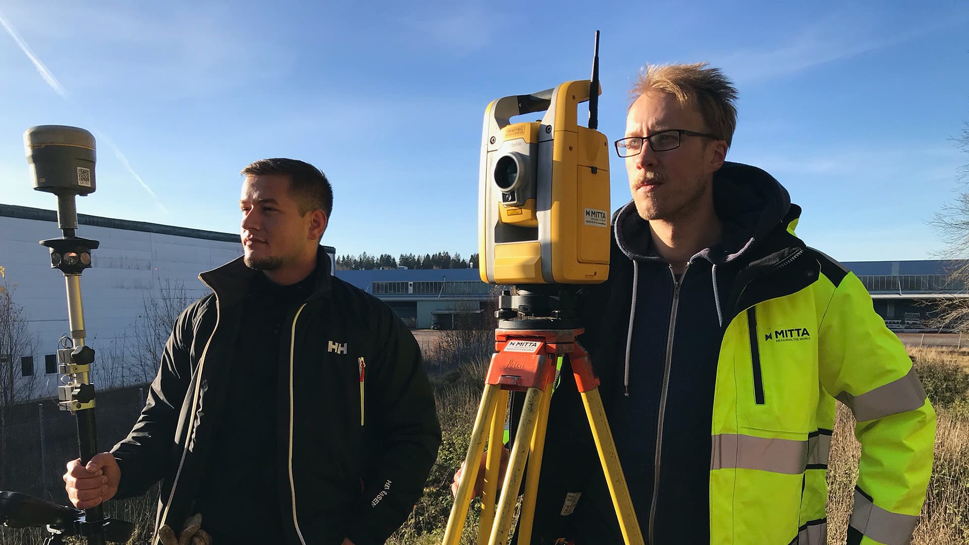 Two men stand outside with surveying service machines